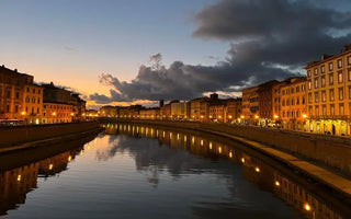 Scenic Italian riverfront at sunset with historic buildings reflected in calm water.